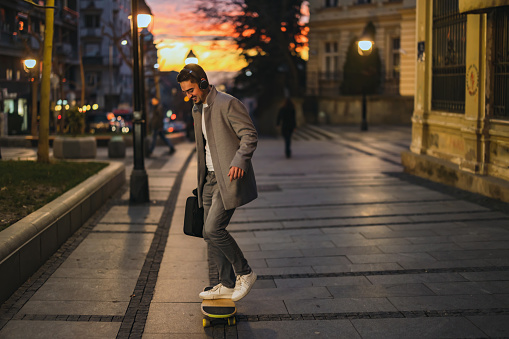 Businessman in the city. Confident young man skateboarding outdoor in suit