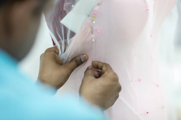 Closeup of male tailor hands pinning and sewing to make a wedding dress. Closeup of male dressmaker pinning and sewing together tulle on a mannequin for a bridal dress. pink gown stock pictures, royalty-free photos & images