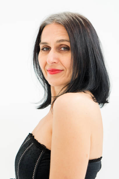 istock Middle aged woman starting getting grey-haired is posing in studio in black clothes and stockings on white background, middle age sexy lady, cosmetology concept 1365928545