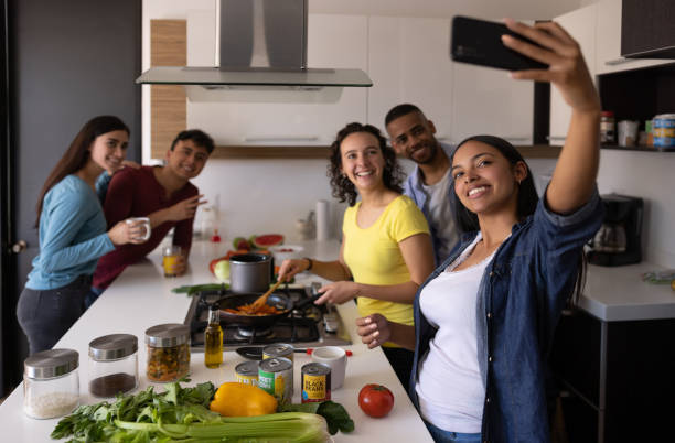Happy group of flat mates taking a selfie while cooking tigether at home Happy group of flat mates taking a selfie with a cell phone while cooking together at home college dorm photos stock pictures, royalty-free photos & images