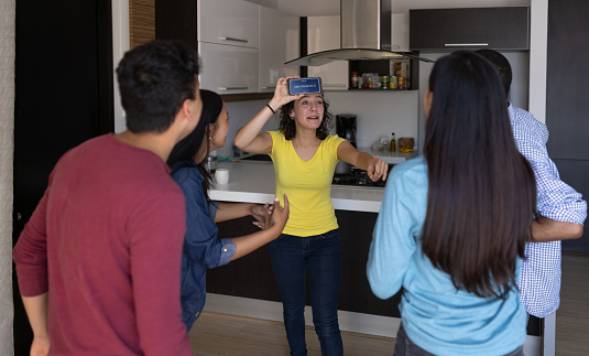 Happy group of friends playing heads up at home using a cell phone - entertainment concepts