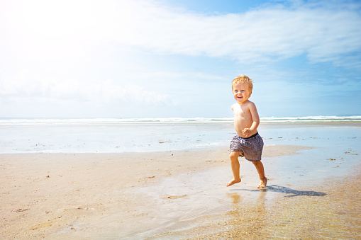Blond toddler child boy run fast on the sand sea beach - motion dynamic image