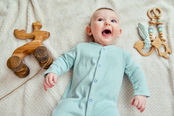 Happy baby lies on a blanket in mint color clothes with wooden toys. Smiling child in turquoise pajamas, top view Happy baby lies on a blanket in mint color clothes with wooden toys. Smiling child in turquoise pajamas, top view newborn horse stock pictures, royalty-free photos & images