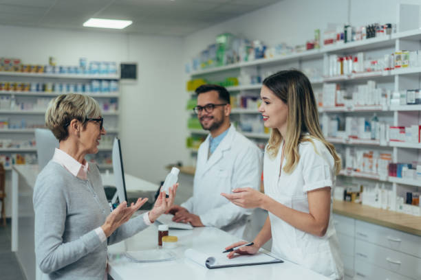istock Male pharmacist working on a computer while female pharmacist is giving prescription medications to senior patient 1365940933