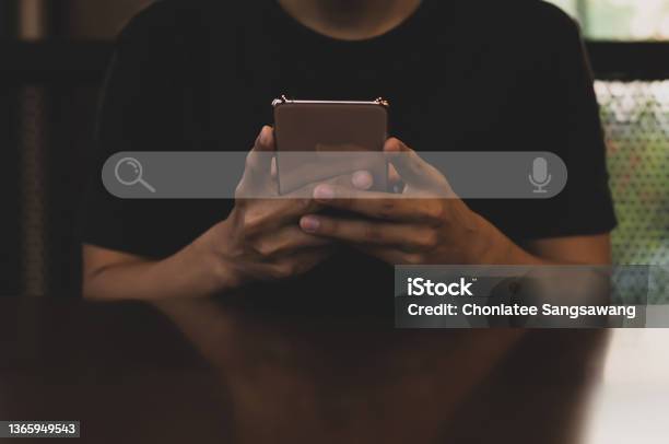 Young Asian Man Wearing Black Tshirt Sitting On Desk Hand Holding Smartphone To Searching For Information Using Search Console With Your Website Stock Photo - Download Image Now
