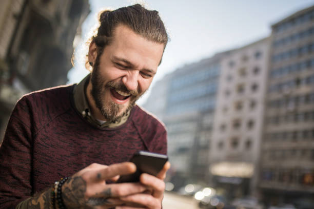 istock Happy young man using phone in the city and laughing. 1365949644