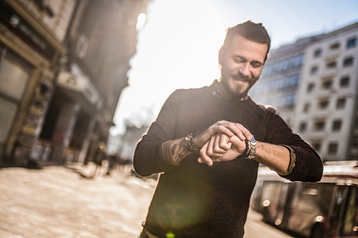 Cheerful young man checking time while walking in the city. Focus on foreground.