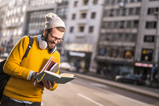 Waist up photo of cheerful young college student standing in the city and checking homework.