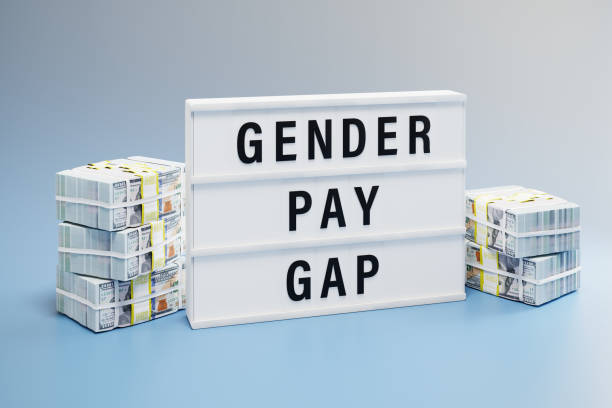 Gender pay gap concept: Two heaps of 100 dollar notes with different height and a lightbox with the words "gender pay gap" inbetween. stock photo