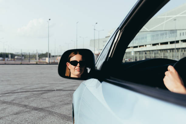 女性は車の中に座って、サイドミラーで殴り、成功し、喜びを感じています - owner women car rear view mirror ストックフォトと画像