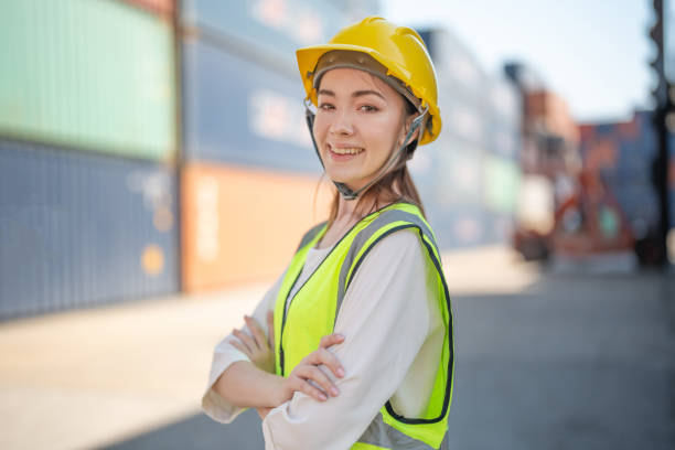 istock factory woman worker is standing with confident with working suit green reflect for safety dress in front container cargo. Concept of smart industry worker operating of shipping transportation. 1365959237