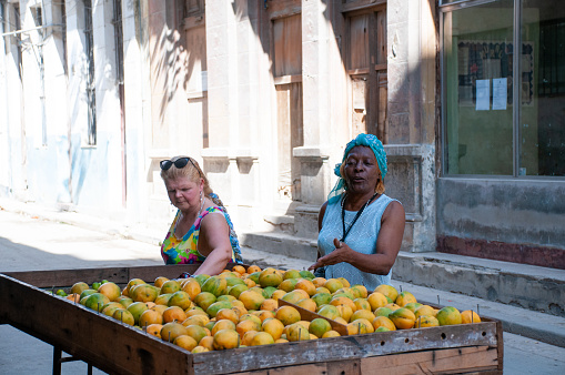 Two women in front of a cart of mangoes for sale on a street in old Havana. Havana. Cuba. May 12, 2015.