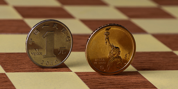 Coins in denominations of 1 American dollar and 1 Chinese yuan stand on the cells of an chessboard