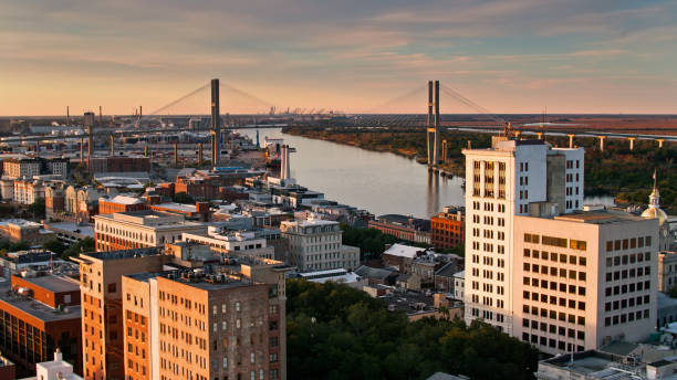 Downtown Buildings on the Banks of the Savannah River - Aerial Aerial shot of Savannah, Georgia at sunset, looking over downtown buildings towards the river, Talmadge Bridge and the distant silhouettes of cranes in the Port of Savannah. georgia us state photos stock pictures, royalty-free photos & images