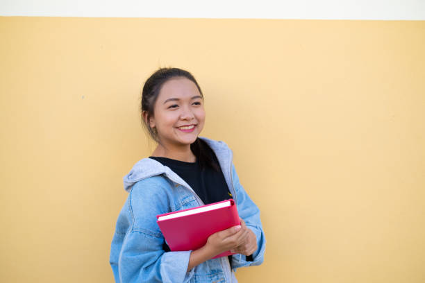 istock Happy student young girl with pink book on brown background. 1365970352