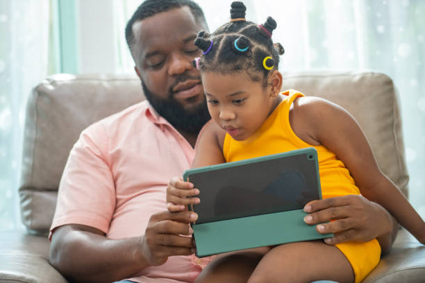 istock African father and little daughter sit on sofa using digital tablet together. 1365972167
