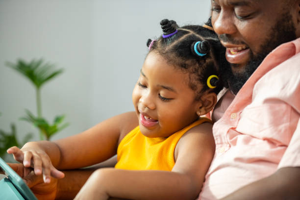 istock African father and little daughter sit on sofa using digital tablet together. 1365972177