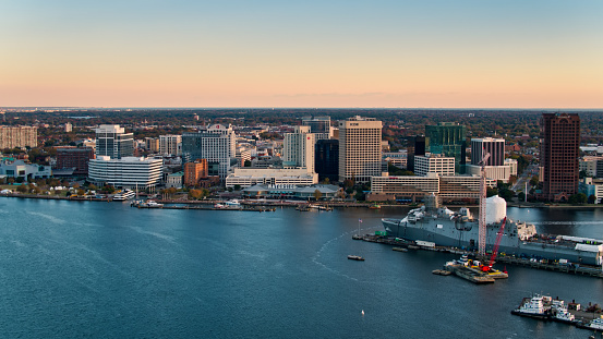 Drone shot of Downtown Norfolk, Virginia from over the Elizabeth River at sunrise, with a warship in a berth on the opposite bank.