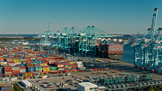 Drone shot of cranes unloading a container ship and straddle carriers loading them onto trucks in Portsmouth Marine Terminal in the Port of Virginia.