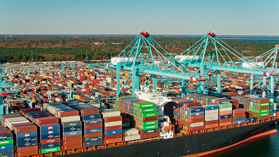 Drone shot of cranes unloading a container ship and straddle carriers loading them onto trucks in Portsmouth Marine Terminal in the Port of Virginia.