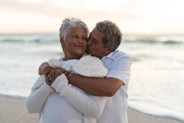 istock Affectionate senior biracial man kissing while hugging woman from behind at beach during sunset 1365976470
