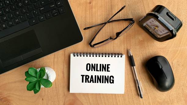 istock Online training text on notebook with laptop, pen, mouse, plant, glasses and brown table background. Online business concept 1365977134