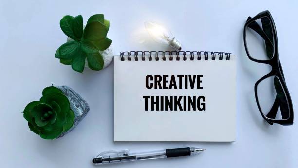 istock Creative thinking text on notepad with glasses, plant, pen and light bulb background. Business concept. 1365977140
