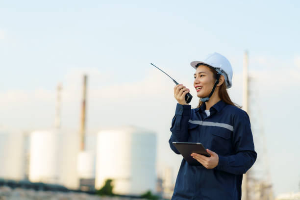 istock Asian woman technician Industrial engineer using walkie-talkie and holding digital tablet working in oil refinery for building site survey in civil engineering project. 1365977294