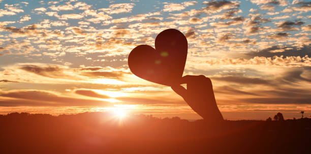 Silhouette of hands holding hearts on sunset sky background. love day concept stock photo
