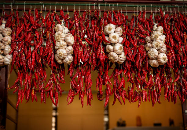 pimientos rojos picantes y ajo cuelgan en un mercado de agricultores - garlic hanging string vegetable fotografías e imágenes de stock