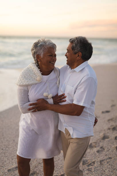 istock Smiling senior biracial couple looking at each other while standing on shore at beach during sunset 1365982053