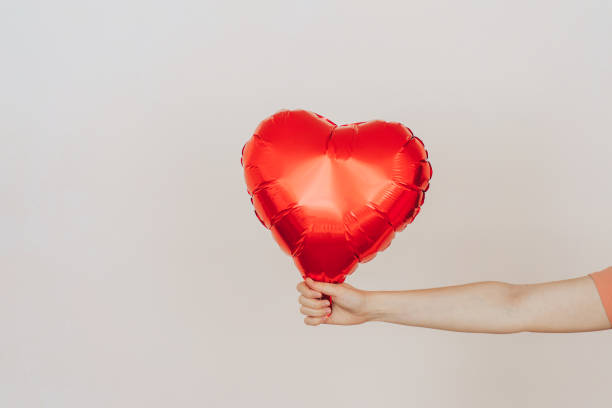 istock Outstretched hand holding heart-shaped balloon against light background 1365982684