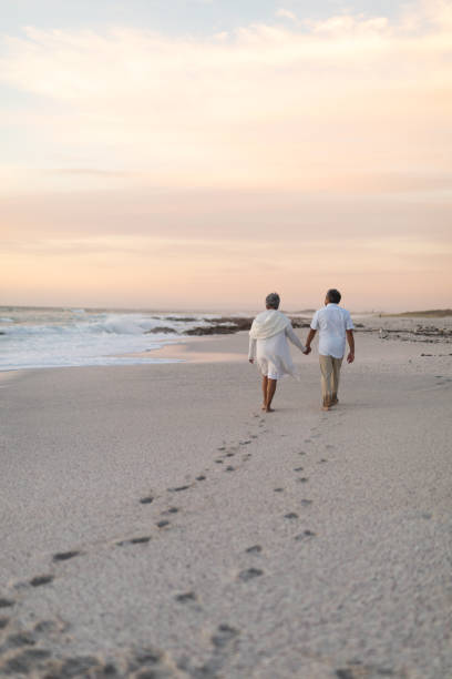 istock Multiracial senior couple walking while leaving footprints on sand at beach during sunset 1365983698