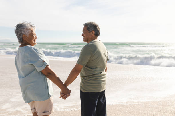 istock Happy retired multiracial senior couple holding hands while looking at each other on sunny beach 1365984858