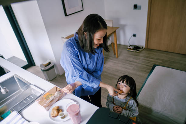 istock Mother feeding daughter while preparing meals for breakfast in the kitchen 1365987151
