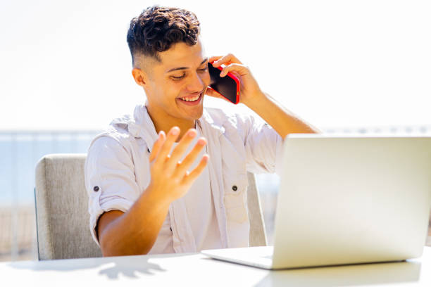 istock man in white t-shirt talking by phone while remote working at sunny beach in cafe 1365988517