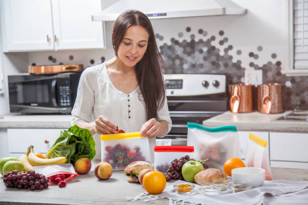 A young mother woman packs strawberries and fresh food into clear storage bags in a modern kitchen stock photo