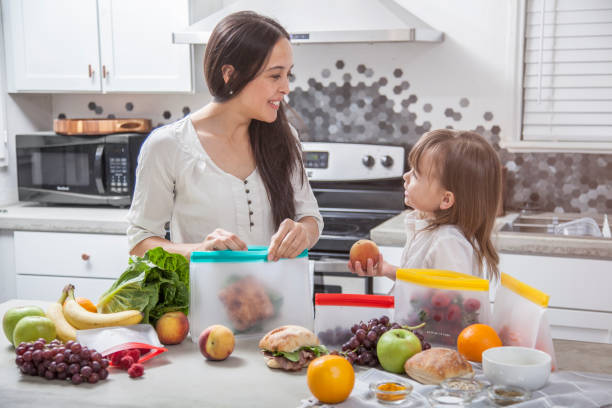 어머니와 딸이 샌드위치와 신선한 음식을 밝은 현대적인 주방의 투명한 수납 가방에 넣습니다. - asian cuisine lunch dinner food 뉴스 사진 이미지