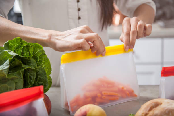 A young mother woman packs carrots and fresh food into clear storage bags in a modern kitchen stock photo