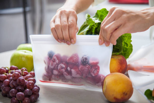 A young mother woman packs frozen raspberries and fresh food into clear storage bags in a modern kitchen stock photo