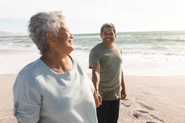 istock Smiling senior multiracial couple holding hands while enjoying sunny day on shore at beach 1365990758