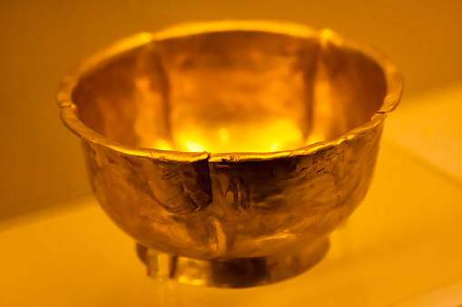 Hand crafted, bronze Tibetan Buddhist Prayer Bell on a white background. The ringer by the side is either used to ring the bell or, to twirl around the base of the bell to make a continuous sound with the help of the pattern on the bell. A face of the Buddha can be seen on the handle.  Photo shot in studio environment; horizontal format.  Copy space.  Close-up.