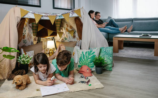 istock Children playing camping at home while their parents read and look at the mobile 1365994474