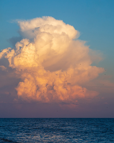 Sky background over the sea. A huge funnel-shaped cloud in the sunset light. An original beautiful cloud over the water.