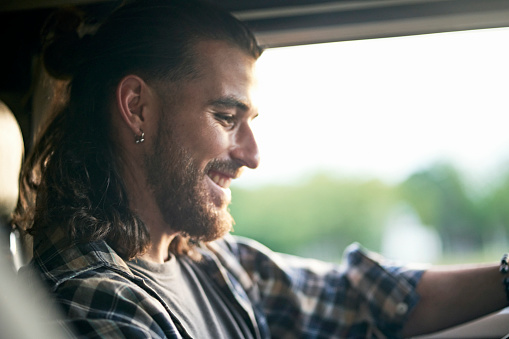 Headshot with profile view of smiling man with medium length hair wearing casual clothing and enjoying road trip.