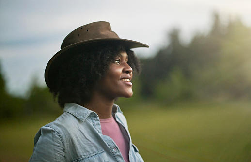 Three-quarter front view of smiling woman with medium-length hair wearing denim shirt, hat, and looking away from camera.