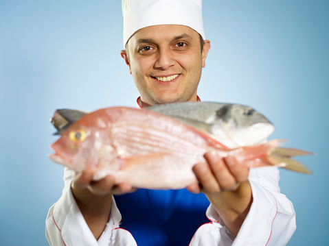 Male chef holding raw fish.