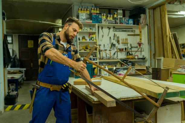 istock Handsome young carpenter cutting the board using the old carpenter saw 1366004091
