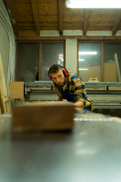 istock Bearded carpenter working on machine for straighten wood boards 1366004836
