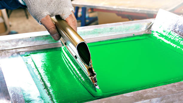 istock silk screen textile printery. male hand with a squeegee. serigraph printing production. creating print on t-shirt in workshop 1366006365